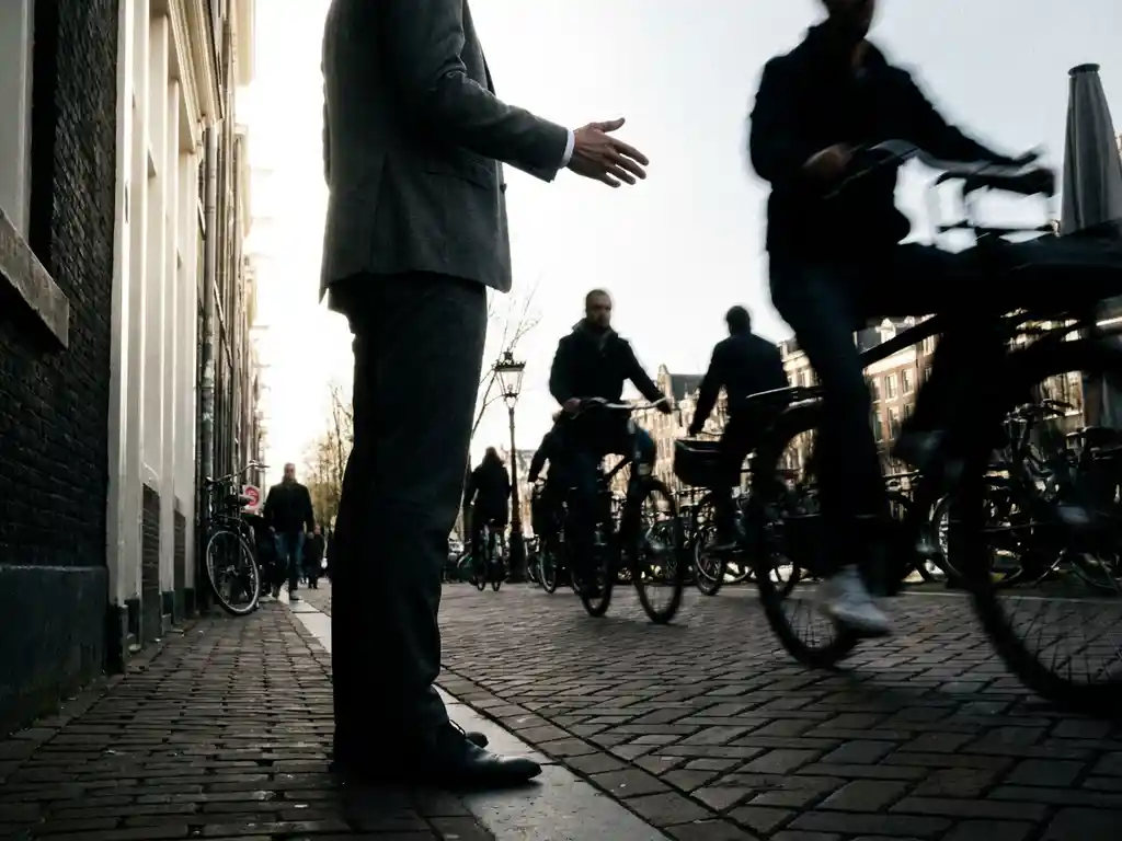 Zelfverzekerde zakenman in pak steekt hand uit op drukke Amsterdamse straat terwijl voorbijgangers onscherp voorbijlopen.