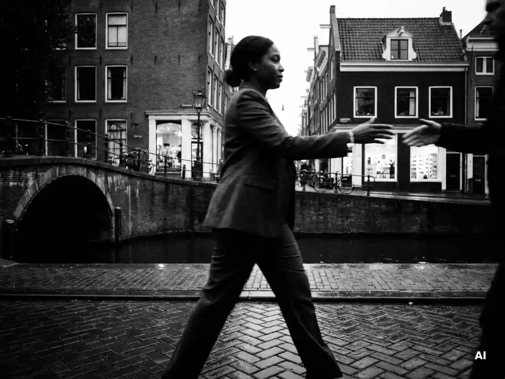 Zelfverzekerde zakenvrouw in blazer loopt doelgericht over natte Amsterdamse kanaalkade, zwart-witfoto met dramatisch lichtcontrast.